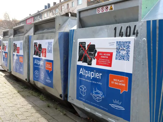 Foto: Altpapiercontainer mit Aufklebern die Tipps und QR Codes enthalten