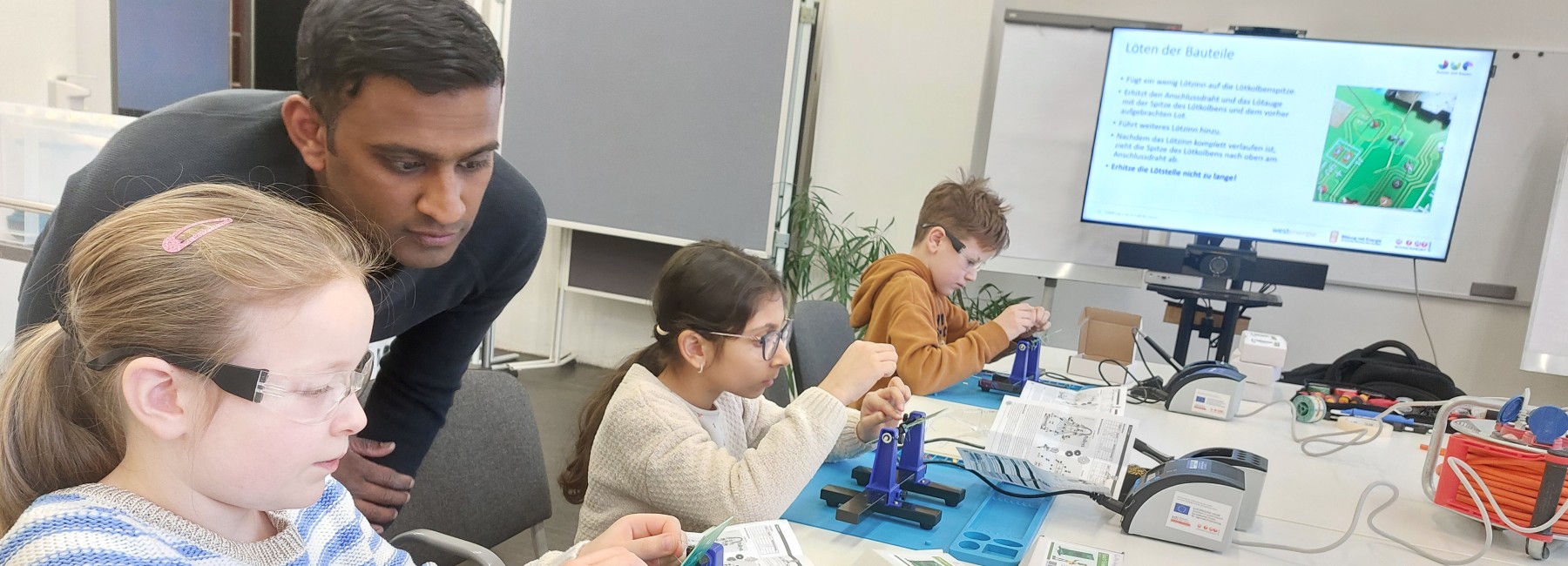 Foto: Kinder arbeiten unter Anleitung an elektronischen Bauteilen