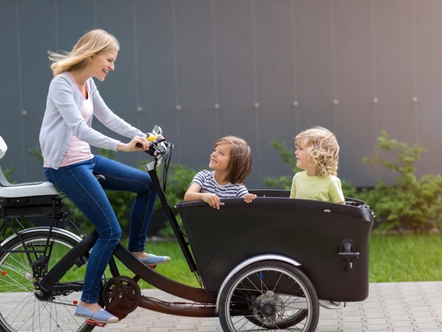 Foto: Kinder sitzen in einem Lastenrad, welches von einer Person gefahren wird