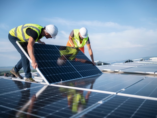Foto: Bauarbeiter verlegen Photovoltaikanlagen am Gebäudedach