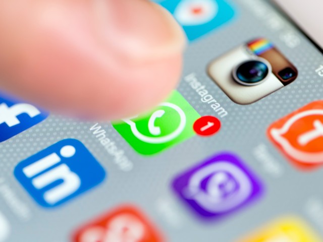 Foto: Display eines Mobiltelefons mit App Icons, ein Finger zielt auf das WhatsApp Symbol