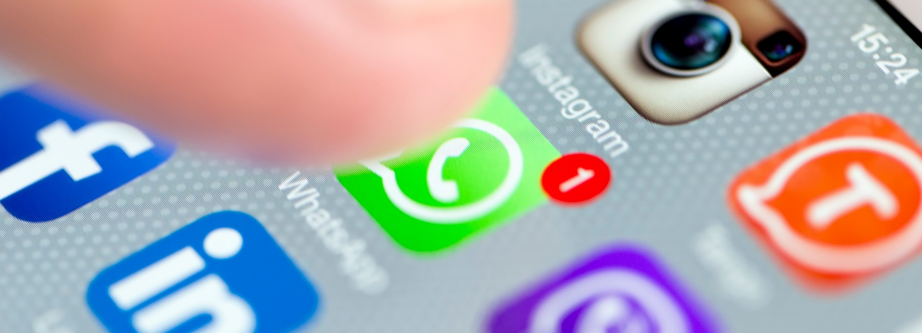 Foto: Display eines Mobiltelefons mit App Icons, ein Finger zielt auf das WhatsApp Symbol