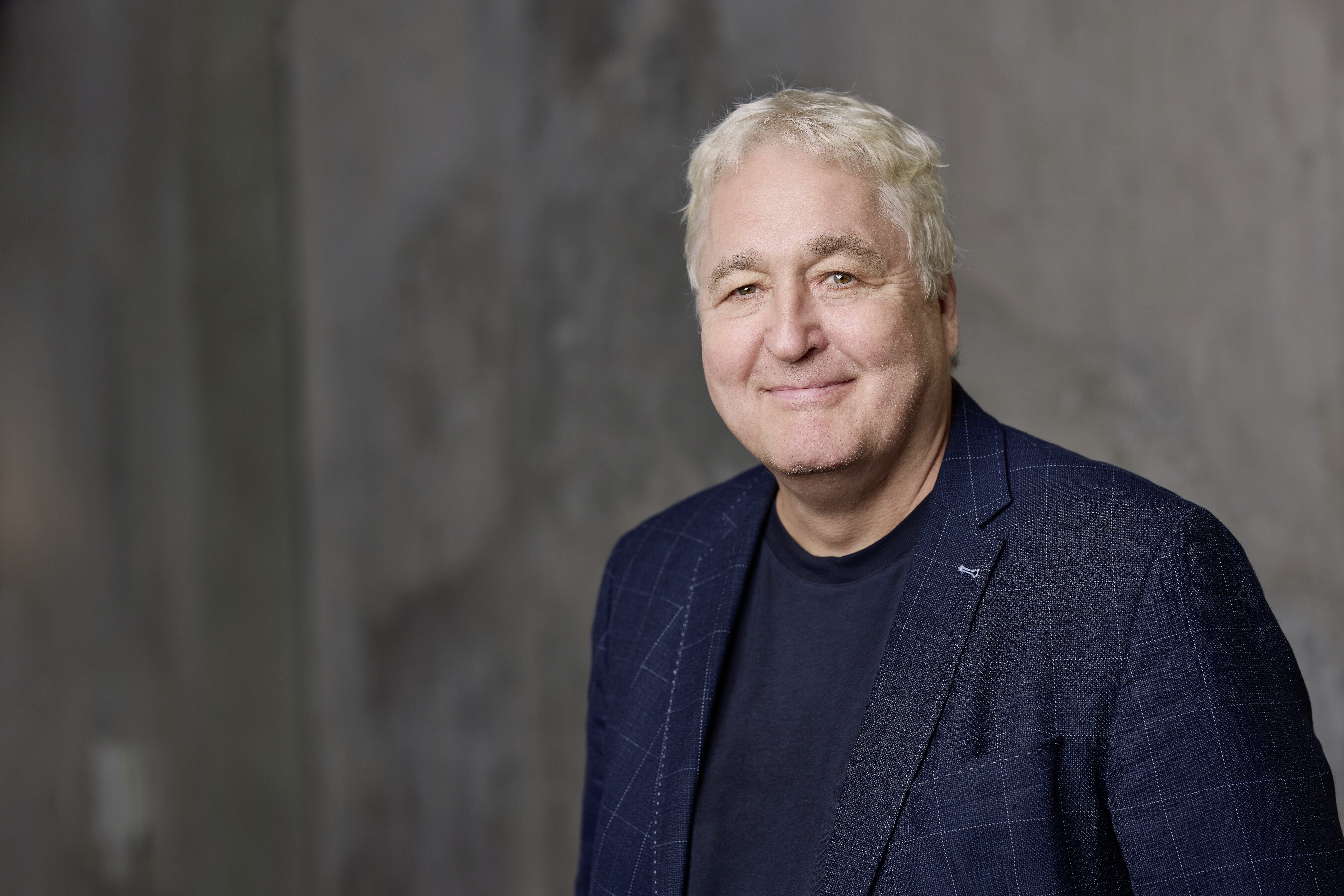 Ein &auml;lterer Mann mit grauem Haar und blauem Jackett l&auml;chelt in die Kamera.