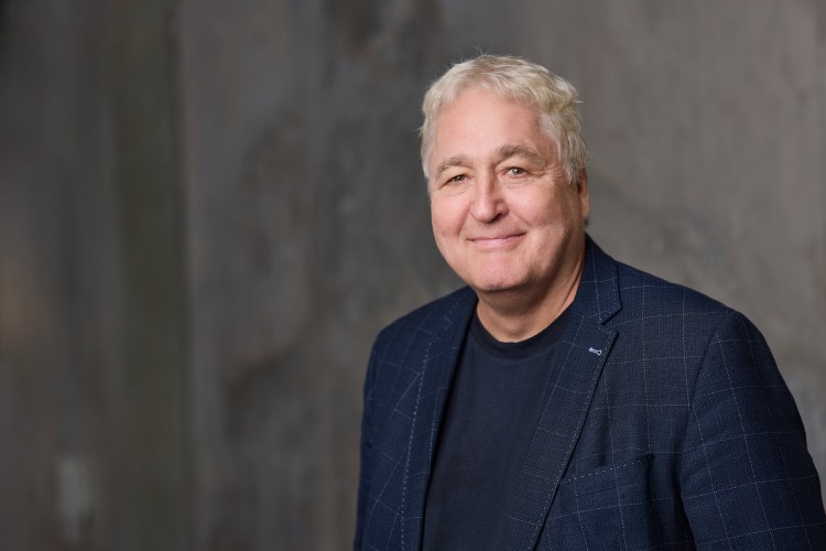 Ein &auml;lterer Mann mit grauem Haar und blauem Jackett l&auml;chelt in die Kamera.