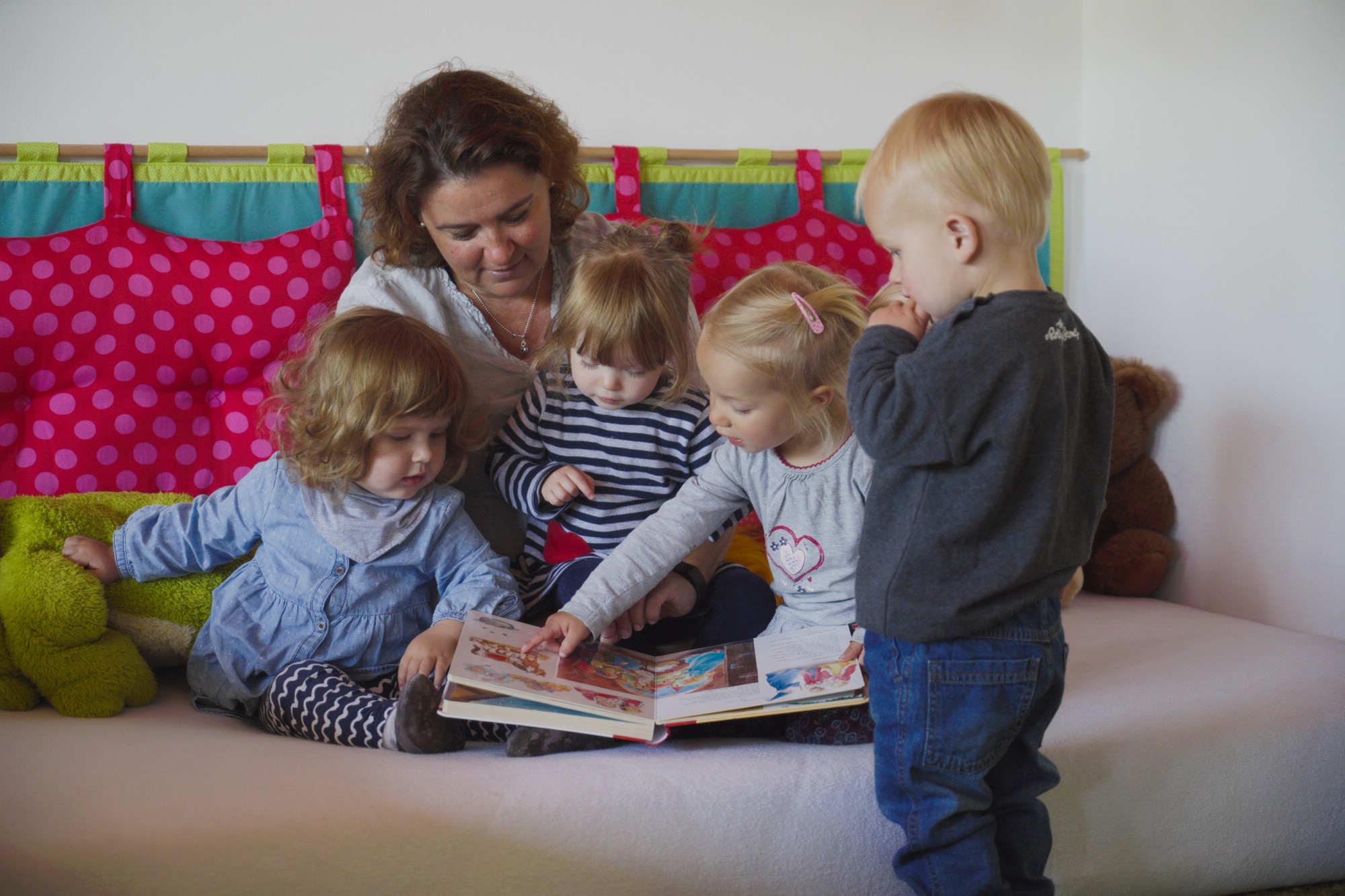 Tagesmutter schaut mit vier Kindern ein Buch an 