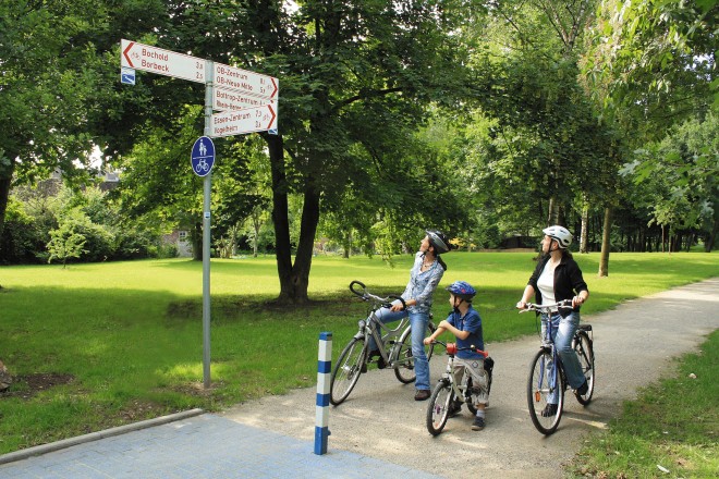 Foto: Zwei Radfahrerinnen und ein Kind schauen auf einen Mast mit Fahrradwegweisern