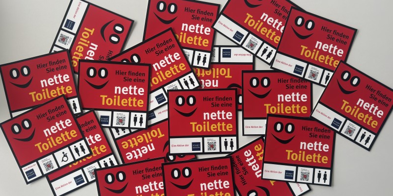 Foto: Mehrere Aufkleber der Netten Toilette liegen übereinander.