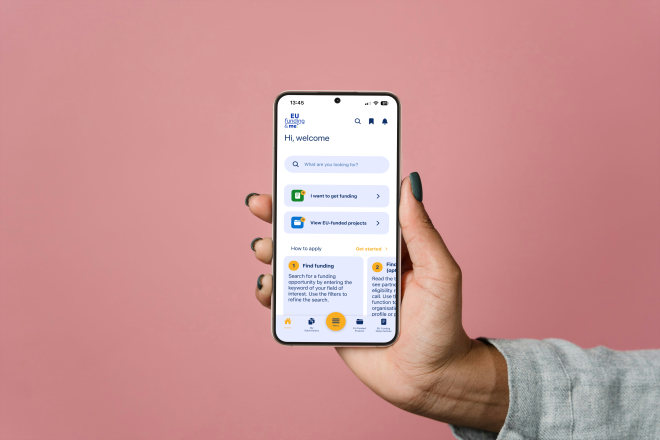 Eine Hand h&auml;lt ein Smartphone in die Mitte des Bildes. Auf dem Smartphone ist die EU Funding & Me-App abgebildet.