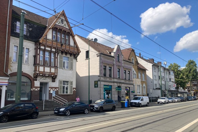 Blick auf eine Häuserreihe an einer Straße mit Straßenbahnschienen - die Sonne scheint und der Himmel ist blau