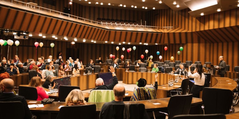 im Ratssaal der Stadt Essen sitzen verschiedene Menschen, im Hintergrund sind bunte Luftballons zu sehen