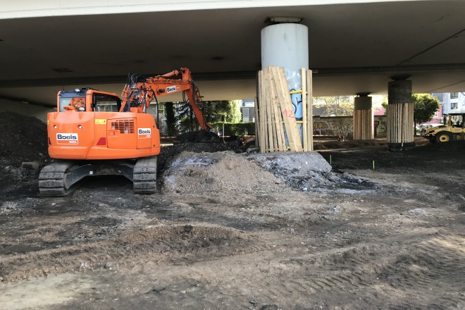 Foto: Blick auf die Baustelle, ein Bagger unter der Brücke mit Stein- und Kieshaufen