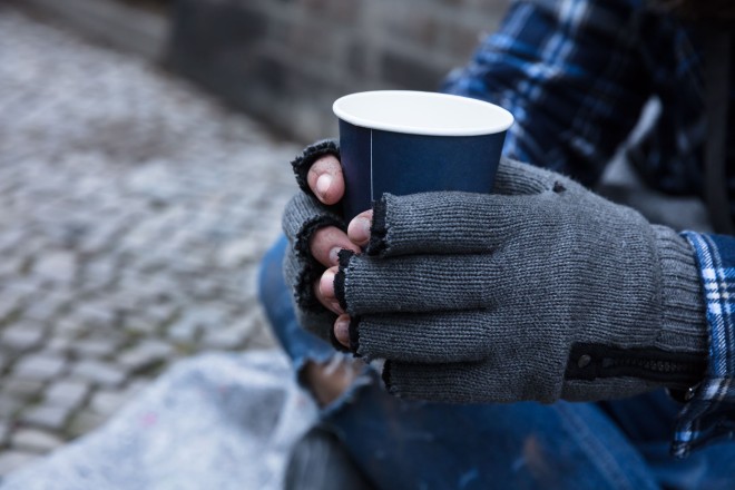 Foto: eine Person sitzt auf dem Boden und hält einen Kaffeebecher in beiden Händen.