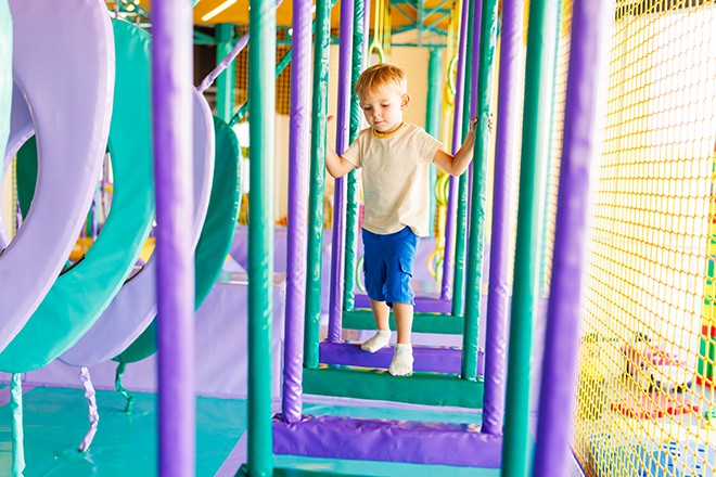 Foto: kleiner Junge, der auf einem bunten Spielplatz im Vergnügungspark spielt.