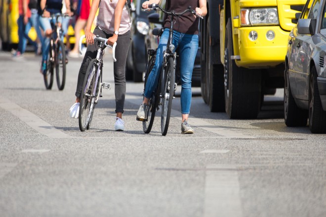 Foto: Eine Straße auf der sich Autos befinden und daneben ist ein Fahrradweg auf dem mehrere Fahrradfahrer unterwegs sind.