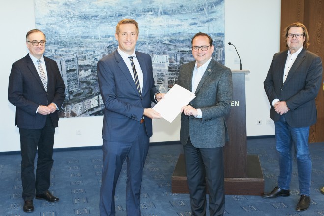 Oberbürgermeister Thomas Kufen nimmt den Bescheid von Thomas Schürmann, dem neuen Regierungspräsidenten des Regierungsbezirks Düsseldorf entgegen. Im Hintergrund links: Beigeordneter Muchtar Al Ghusain und rechts: Stadtkämmerer Gerhard Grabenkamp.